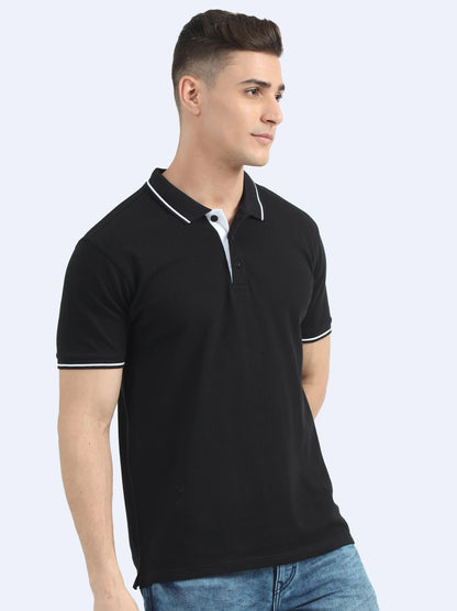 Man wearing black polo t-shirt with white collar trim and blue jeans on plain background