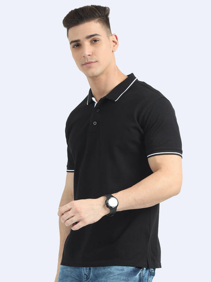Man wearing black polo t-shirt with white trim, blue jeans, and a black wristwatch