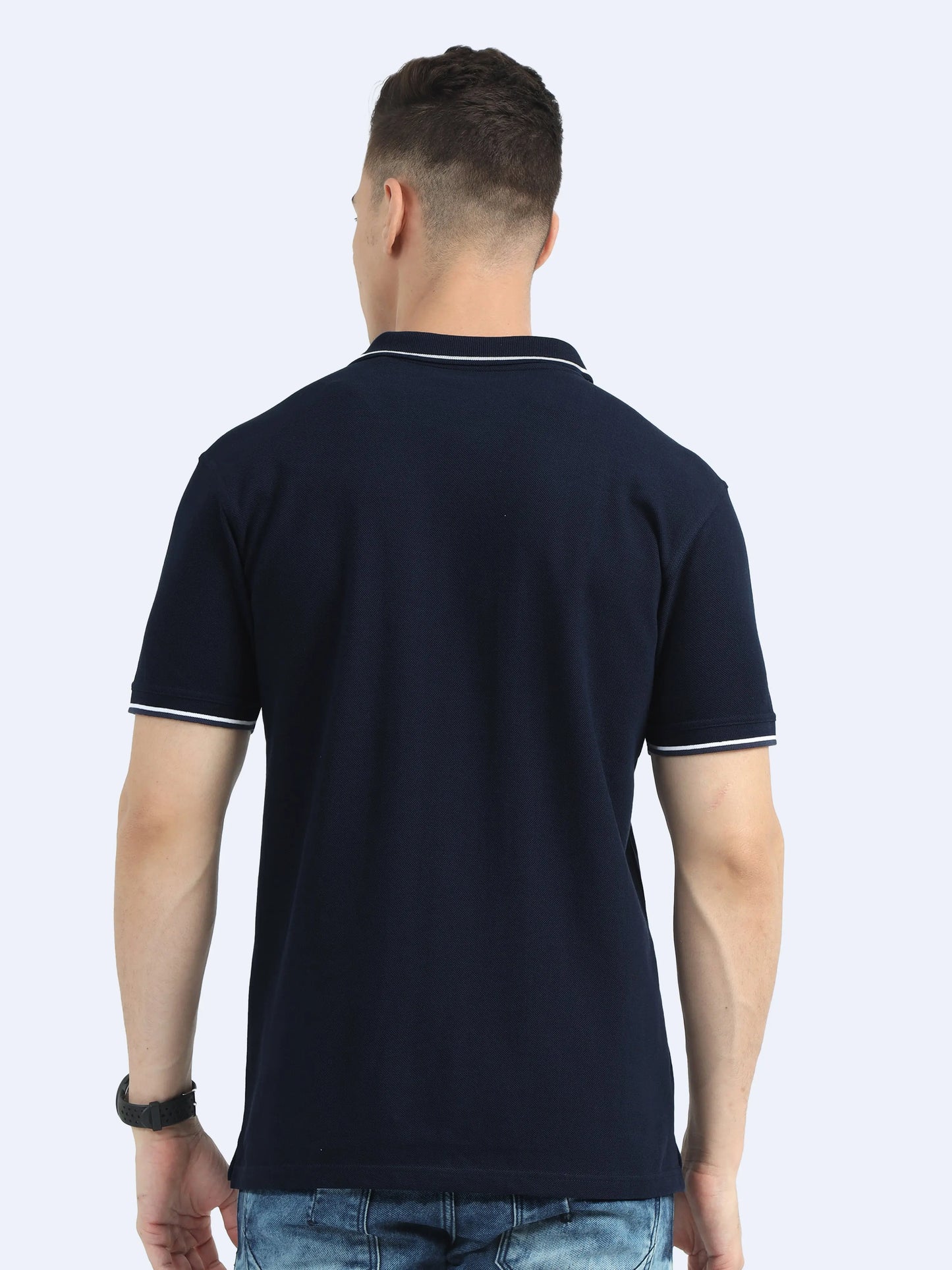 Back view of man wearing navy blue polo t-shirt with white trim, casual jeans