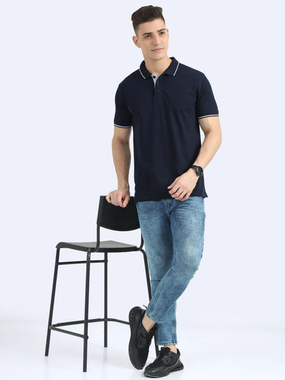 Man in navy blue polo t-shirt and blue jeans standing by a chair, casual corporate apparel