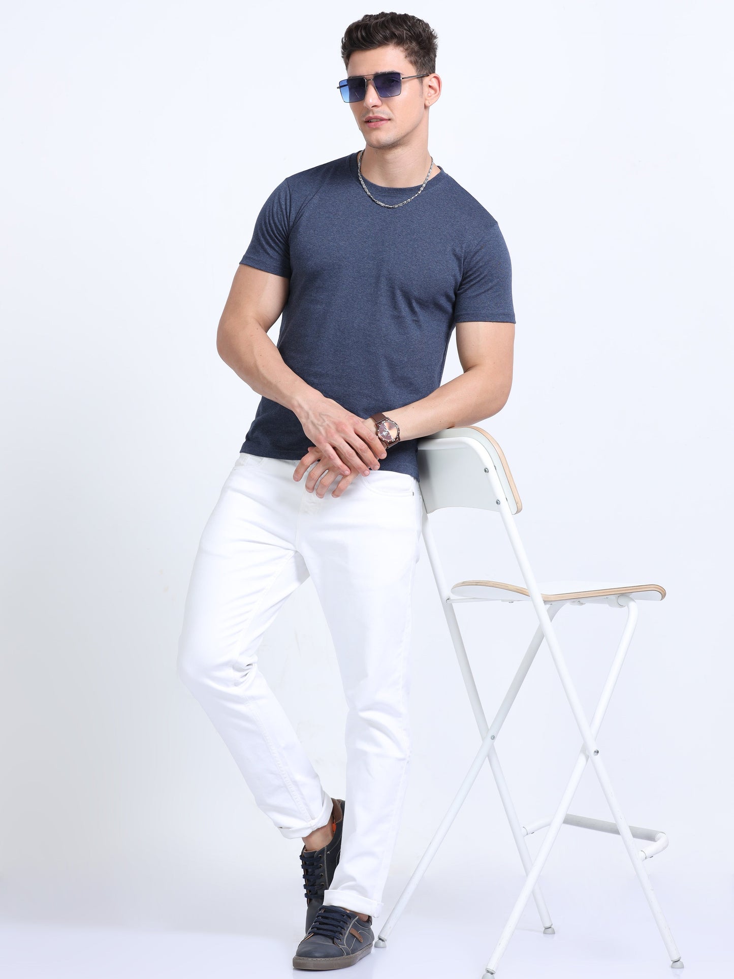 Man in navy blue t-shirt and white pants posing with chair, corporate casual style