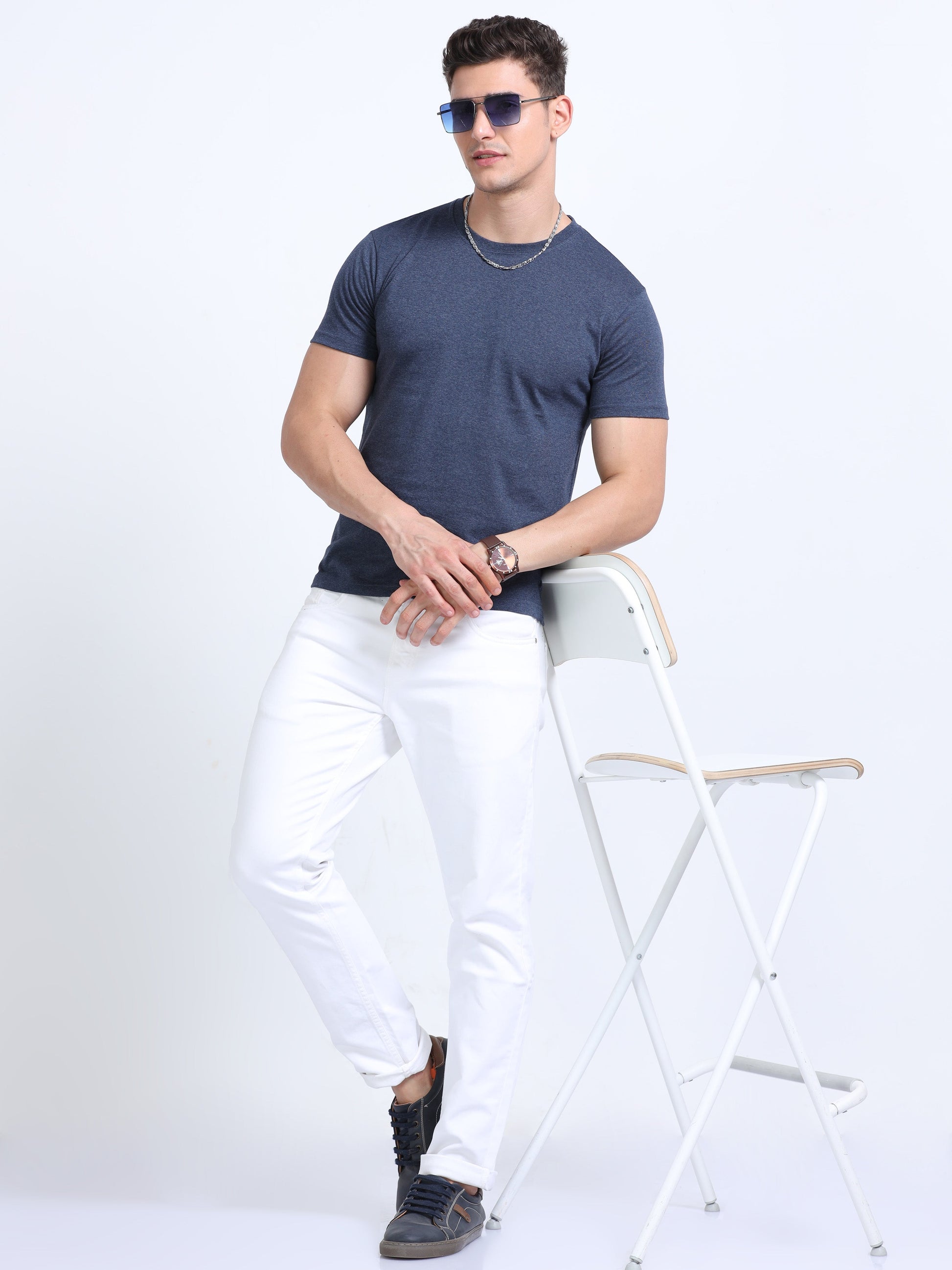 Man in navy blue t-shirt and white pants posing with chair, corporate casual style