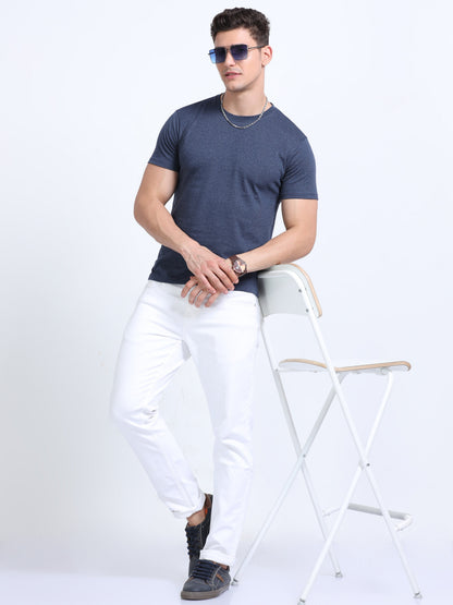 Man in navy blue t-shirt and white pants posing with chair, corporate casual style