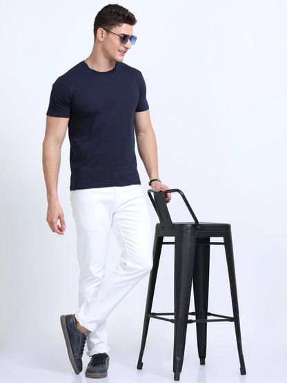 Man in navy blue t-shirt and white pants posing with black bar stool, stylish apparel